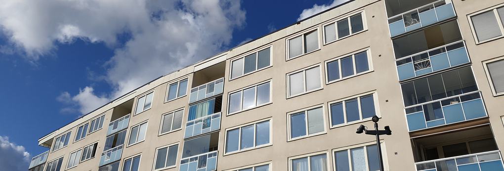 Närbild på vitt lägenhetshus med blå balkonger.