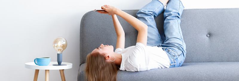 En tjej ligger på en grå soffa med benen mot väggen, och hennes hår utsläppt som faller mot golvet.