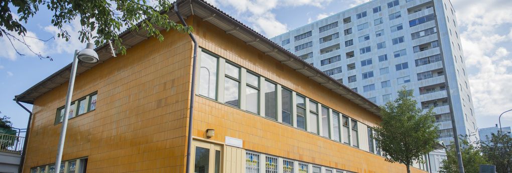 En byggnad med fasader av orange tegel en solig dag, ljusblått flerfamiljshus i bakgrunden.