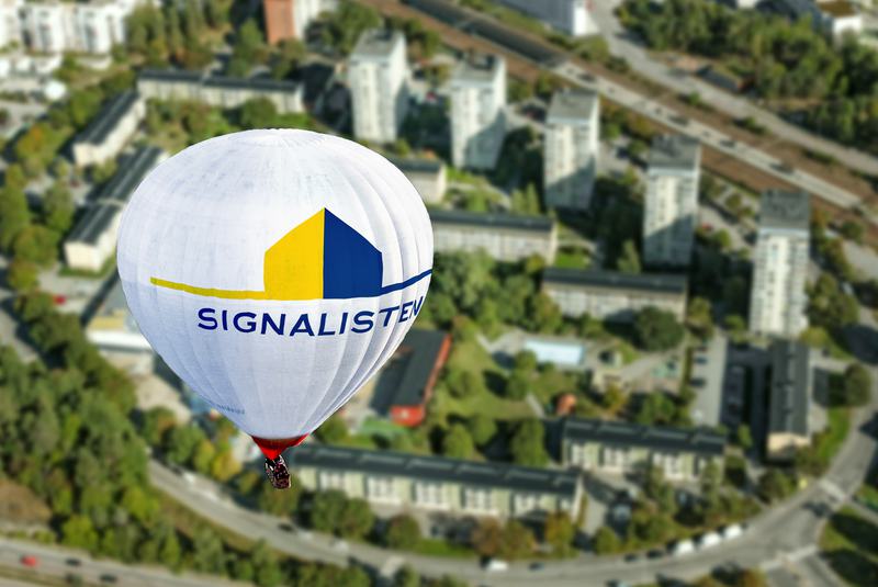 Varmluftsballong med Signalistens logotyp svävar högt över stadsbebyggelse