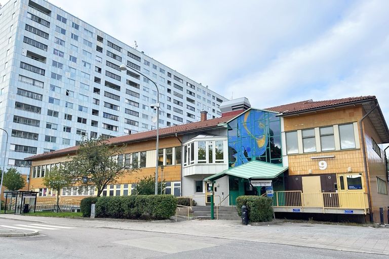 Bild på suterränghus i orange kakel med ljusblått högre flerfamiljshus i bakgnden, gröna träd runt om och mindre gata framför.