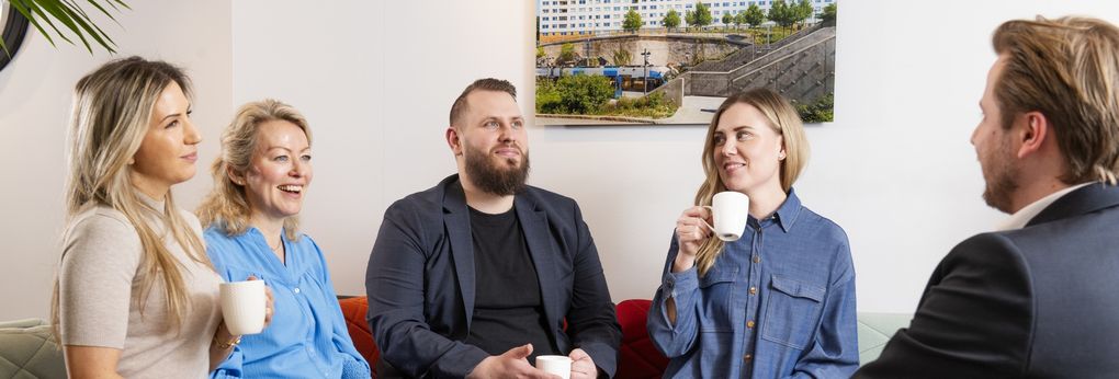 Fem personer som sitter och pratar över fika.