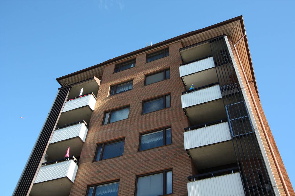 Del av brunrött lägenhetshus med vita balkonger.