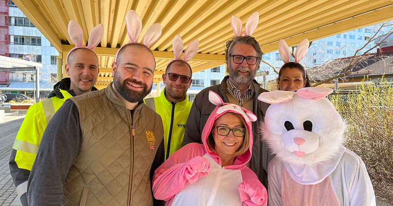 Sju personer under ett gult tak varav två är utklädda till påskharar och resten har diadem med kaninöron på sig.