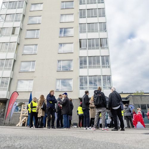 Folksamling framför ett höghus i ljusa färger.