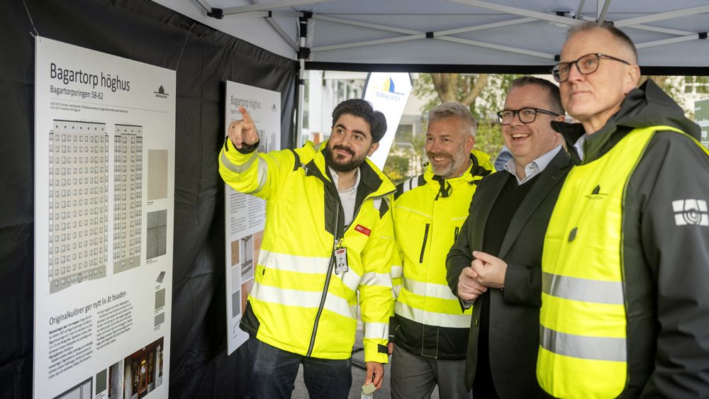 Fyra män i skyddsvästar tittar på en skiss över Bagartorp höghus.