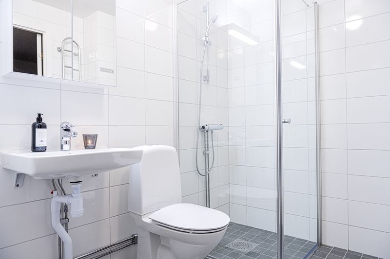 Badrum med mörkgrått golv, vita väggar och glasvägg till dusch.