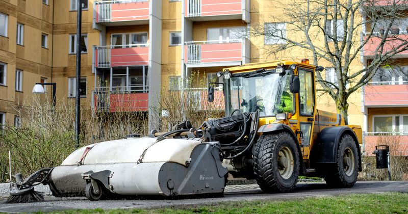En stor maskin som används för att sopa bort sand på en innergård till ett bostadsområde.