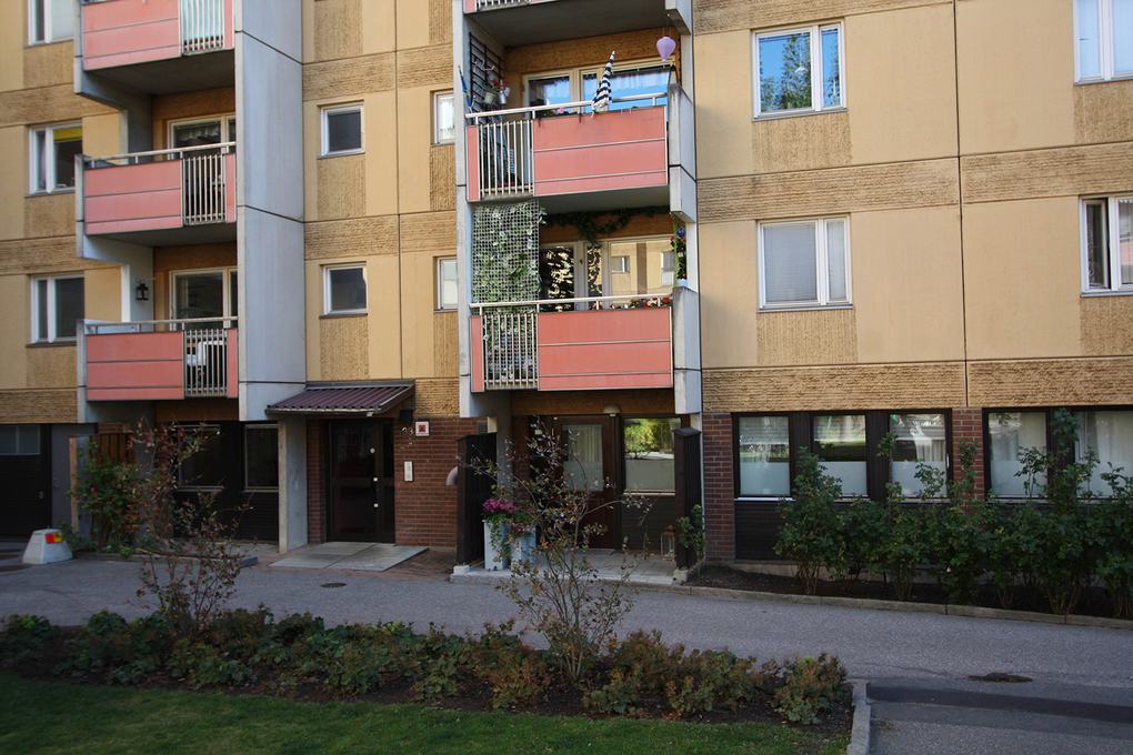 Gult lägenhetshus med röda balkonger i närbild.