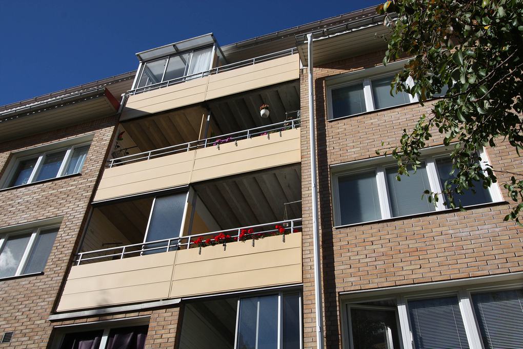 Närbild på lägenhetshus i tegel med gula balkonger under tak.