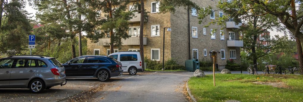 Tre bilar står på en parkeringsplats vid ett flerbostadshus.