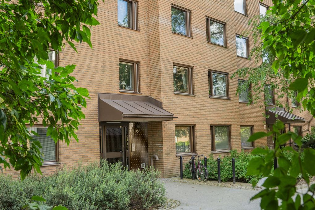 Port till ett brunt tegelhus omgivet av grönska. Ett cykelställ intill porten.