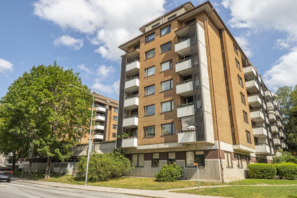 Brunt flervåningshus i tegel med vita balkonger mot en gata.