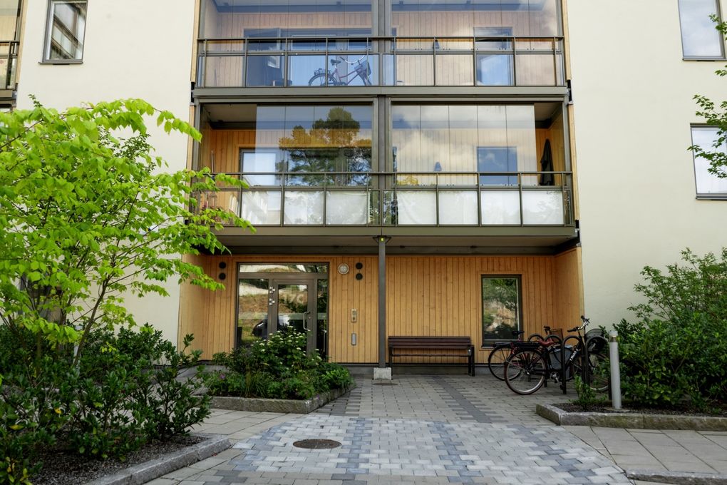 Närbild på port i trädetaljer till ett vitt flervåningshus med inglasade balkonger.