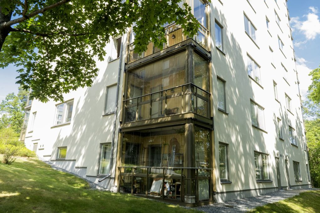 Vitt höghus med inglasade balkonger mot en gräsmatta.