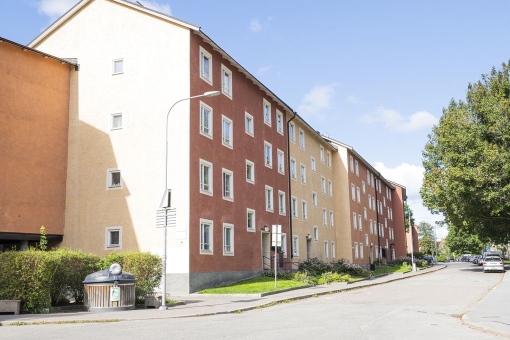 Flerbostadshus i röda och gula nyanser i tre våningar mot en gata.