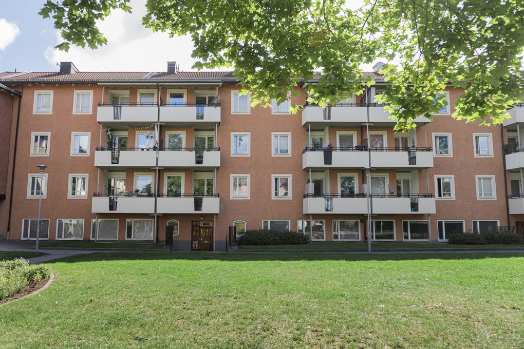 Ljusrött flerbostadshus med tre våningar och balkonger mot en innergård.