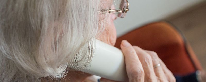 Äldre persons huvud syns bakifrån och och håller en telefonlur mot örat.
