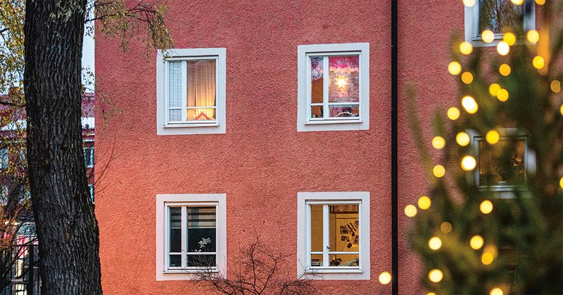 Röd husfasad där man ser fyra fönster, en julgran i förgrunden.