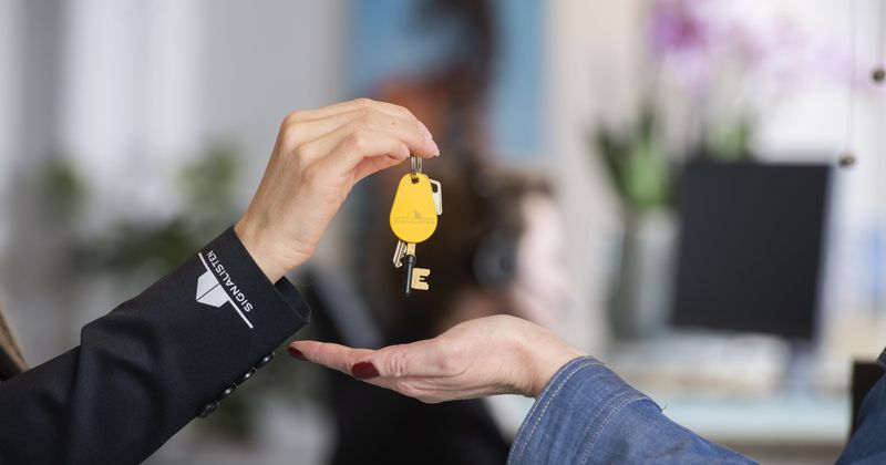 En hand som lämnar en nyckelknippa med en gul passertagg och två nycklar på till en annan hand.