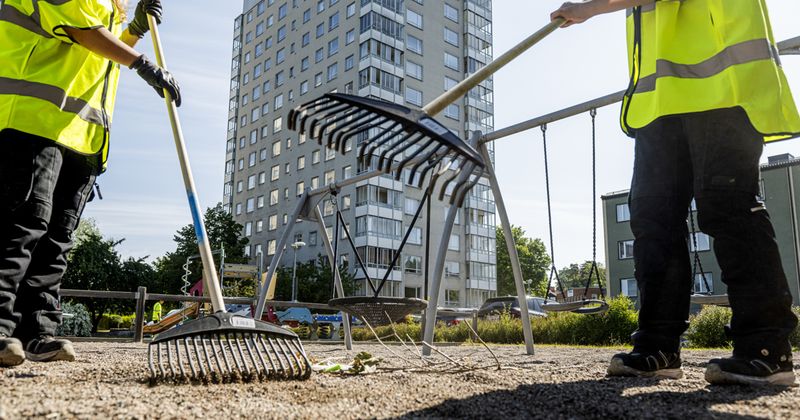 Två personer som krattar på en lekplats i ett bostadsområde.