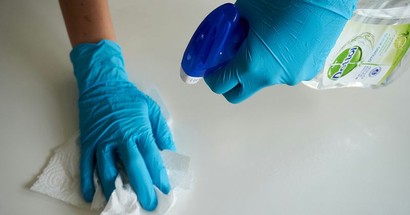 Händer med städhandskar på som sprayar städmedel och torkar av en yta.