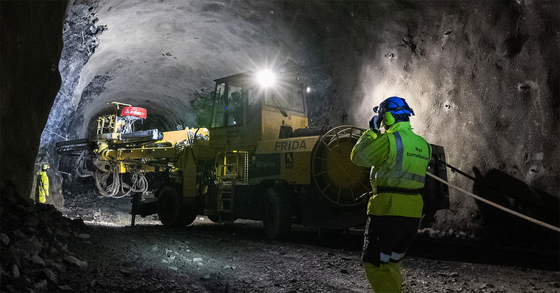 En person i arbetskläder nere i en tunnel. I bakgrunden står en schaktmaskin.